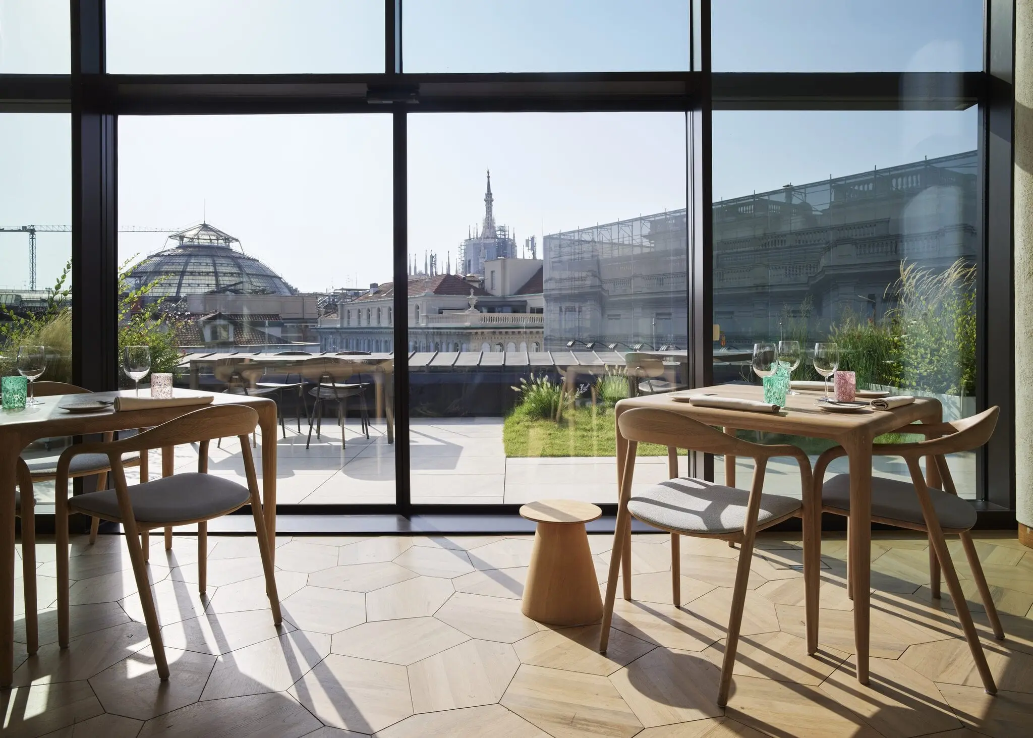 Sala con vetrate su terrazza e Duomo, tavoli apparecchiati e Galleria sullo sfondo